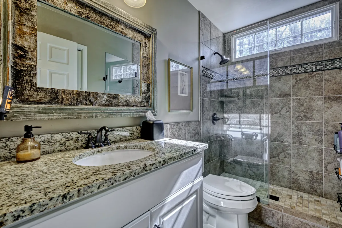 A stylish bathroom featuring a gleaming granite countertop, a spacious glass shower enclosure, and a large mirror reflecting soft, inviting light. The space feels both fresh and restful—ideal for unwinding after a day spent outdoors.