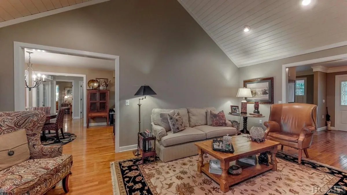 A welcoming living room with a plush sofa facing a coffee table, accompanied by a decorative chair and a softly glowing lamp. The space is arranged for relaxation and socializing, creating an intimate environment for group gatherings.