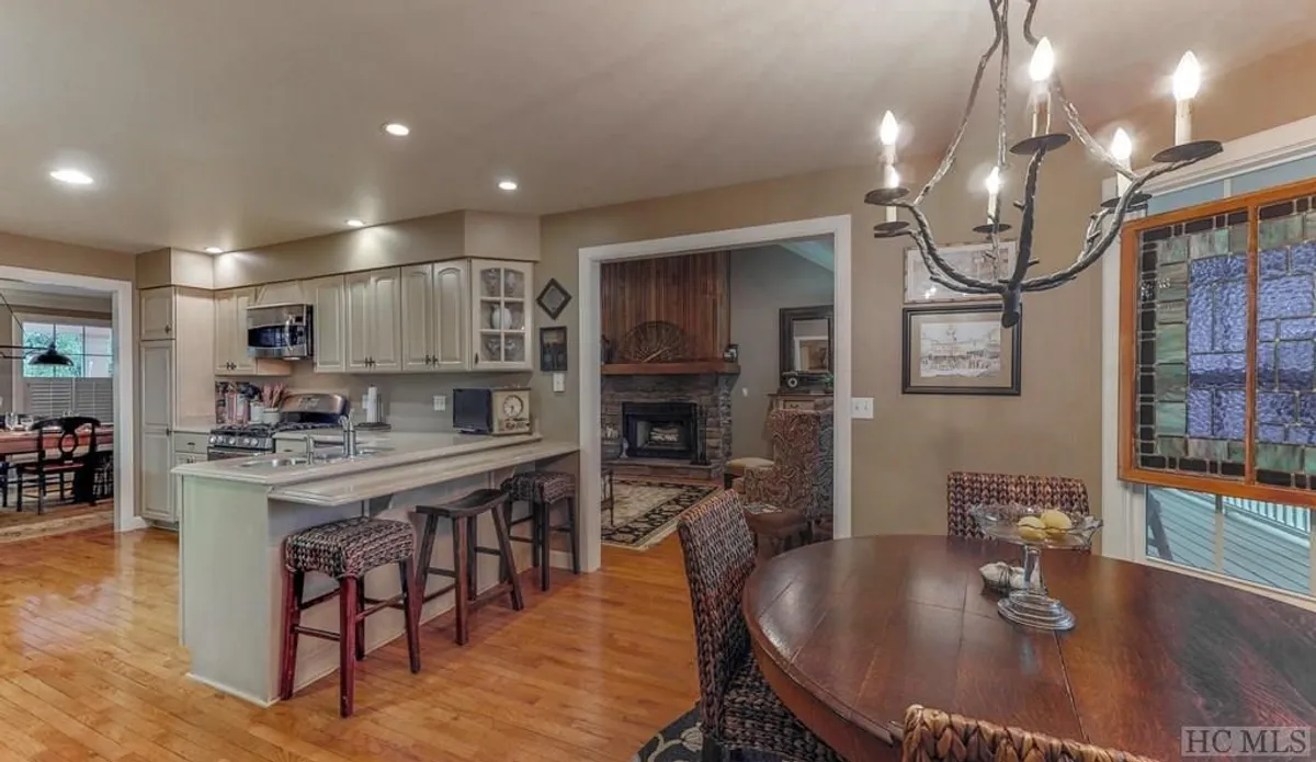 An open-concept area featuring a kitchen island, a large dining table, a glowing fireplace, and a colorful stained glass window. The arrangement offers seamless transitions between cooking, dining, and relaxing by the fireside, encapsulating the home's communal spirit.
