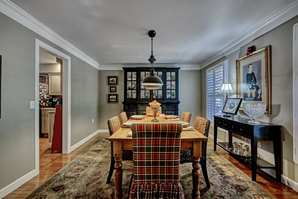 A warm, inviting dining room anchored by a central dining table, accented by a black hutch, plaid table runner, and tasteful wall art. The setup suggests an ideal space for family meals, holiday gatherings, or dinner parties, conveying a sense of tradition and conviviality.