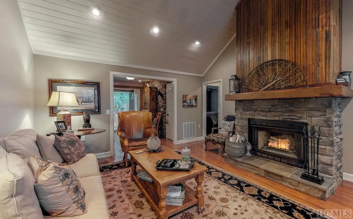 The image showcases a warm, inviting living space centered around a stone fireplace. Plush armchairs and a stylish coffee table create a cozy gathering spot, perfect for relaxing with a book or sharing stories over hot cocoa. The overall mood is welcoming and intimate, with thoughtful décor and comfortable furnishings enhancing the atmosphere.