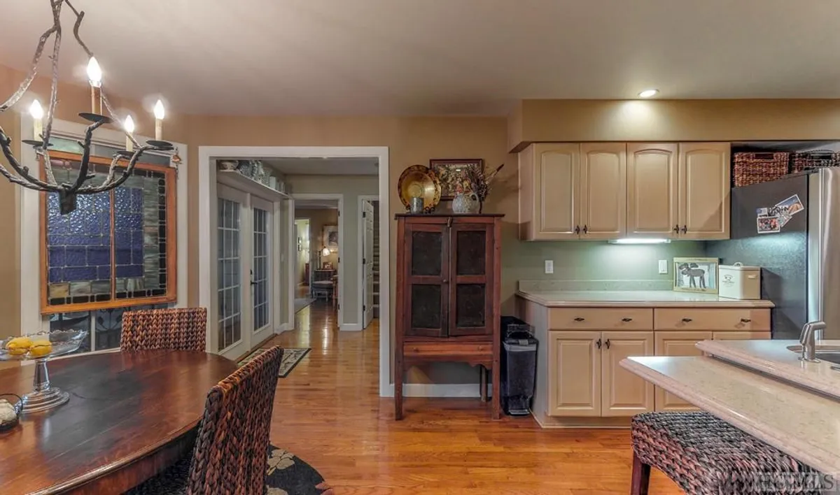 This interior image features a dining table set beneath an elegant chandelier, with the kitchen counter and cabinetry visible in the background. A stained glass window adds character while subtle decor cues suggest the space is ready for both everyday meals and festive gatherings.